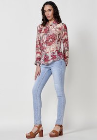 Blusa trasparente a maniche lunghe con motivo paisley rosso e blu; abbinata a jeans fitted azzurri e sandali con zeppa in legno marroni.
