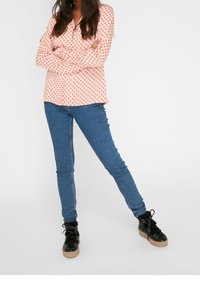 Camicia a maniche lunghe di un rosa chiaro con pois rossi, abbinata a jeans skinny blu e sneakers alte nere con suola beige.