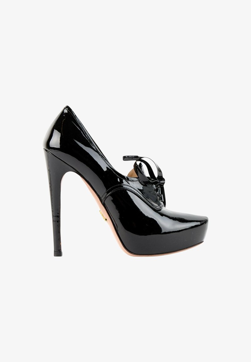 Chaussure à talon haut en cuir verni noir avec une semelle plateforme et un nœud décoratif sur le dessus, vue de côté sur fond blanc.