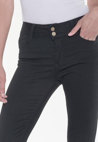 Jeans de mezclilla negra con un diseño ajustado, que cuentan con cierre de doble botón y bolsillos frontales. Textura lisa, sin patrones visibles ni desgastes.