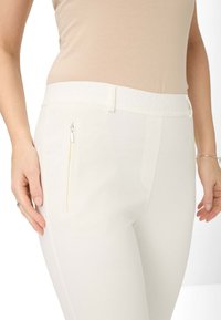 Pantalons blancs avec une taille élastique texturée. Dotés d'une poche zippée sur le côté et d'un tissu lisse, conçus pour le confort et la flexibilité.