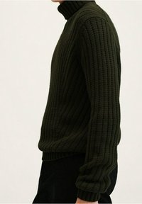 Donkergroene gebreide coltrui met geribbelde textuur, lange mouwen en een aansluitend model.