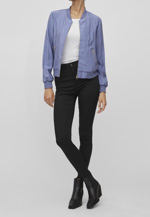 Lys lilla bomberjakke med en glat tekstur, ribbede manchetter og lynlåslommer, parret med sorte strammende jeans og ankelstøvler.