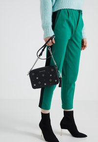 Borsa nera con decorazioni a forma di stella, hardware argentato, tracolla a catena e nappina; abbinata a pantaloni teal e stivaletti neri a costine.