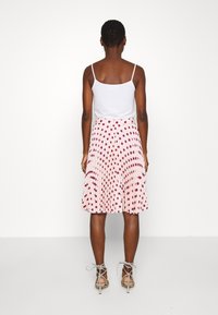 Rok midi plissée berwarna merah muda muda dengan titik polkadot merah tua. Dipadukan dengan tank top putih yang pas dan sandal hak tinggi berwarna abu-abu dengan tali.