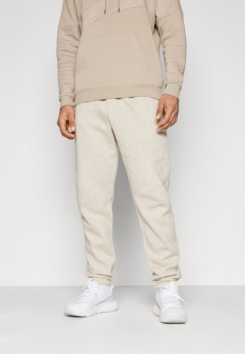 Beige sweatshirt met een gestructureerd bovenpaneel, zak aan de voorkant en een trekkoord. Bijpassende beige joggingbroek met een zachte textuur en elastische boorden. Witte schoenen.