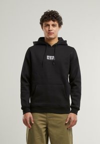 Čierny flísový hoodie s predným kloktacím vreckom, šnúrkami a bielym logom "USA" na hrudi. Tkanina je hladká a jemná.