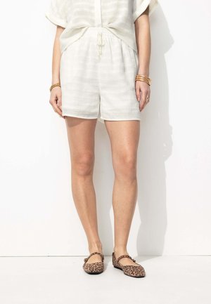 Shorts blancs texturés à taille élastique associés à des ballerines à imprimé léopard. Les shorts sont dotés d'un cordon de serrage et de poches latérales. Design minimaliste.