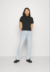 Black fitted t-shirt with short sleeves and a round neckline, paired with light blue flared jeans and black ankle boots. Plain background.