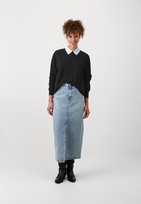 Suéter negro con cuello blanco, combinado con una falda larga de mezclilla azul claro y botas negras hasta el tobillo. Diseño simple y limpio con elementos casuales.