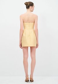 Robe sans bretelles en tissu doré texturé, évasée à partir de la taille. Dotée d'une fermeture à glissière au dos et d'un corsage ajusté.