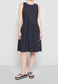 Vestido sin mangas de color azul marino con cintura fruncida, tejido fluido y falda hasta la rodilla. Combinado con sandalias de plataforma a rayas en azul marino y blanco.