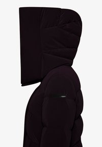 Giacca a vento nera con cappuccio oversize, design trapuntato, materiale spesso e vestibilità slim. Presenta una patch con il logo sulla manica.