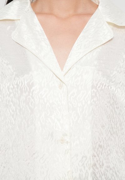 White, textured shirt featuring a subtle pattern, a pointed collar, button closure with a single button visible, and a light, sheer fabric.
