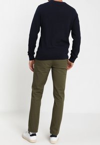 Marinblå tröja, långa ärmar, rundad halsringning; olivgröna byxor, smal passform, ankellängd; vita sneakers med marinblå detaljer.