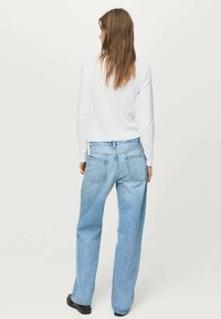 Jeans de culoare albastră deschisă, cu croială largă și talie înaltă, cu cinci buzunare și un finisaj decolorat, asortați cu un top alb cu mânecă lungă.