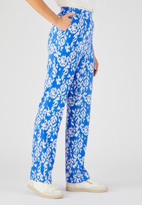 Blauwe patroon broek met wit bloemenontwerp, elastische tailleband, zijzakken en een rechte pasvorm, gedragen met lichtgekleurde sneakers.