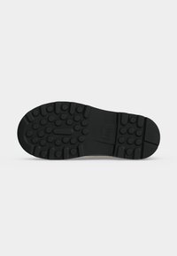 Semelle de chaussure en caoutchouc noir avec des motifs de bande de roulement ronds et rectangulaires, comprenant des clous circulaires surélevés pour la traction.