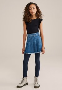 Črn prilegajoč top z volančki na rokavih, denim krilo z naborki in raztrganim robom, temno modre legice ter svetlo sive čevlje z vezalkami.