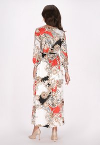 Maxime dress dengan pola bunga dan paisley berwarna merah, hitam, dan emas di latar belakang putih, dengan lengan panjang dan pinggang yang cinch.