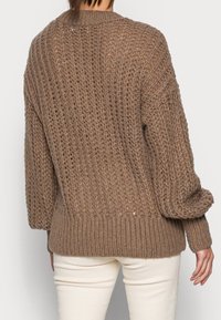 Brązowy sweter z dzianiny o luźnym kroju, teksturowanym wzorze, ściągaczu u dołu i przy mankietach. Materiał wydaje się miękki i gruby, z luźną sylwetką.