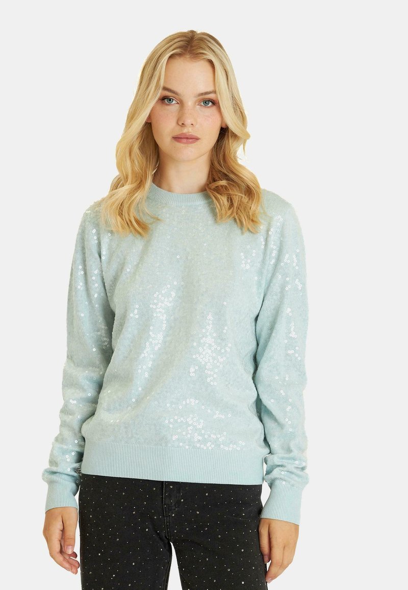 Jasnoniebieski sweter z cekinami pokrywającymi przód, prążkowanymi mankietami i dolnym wykończeniem, okrągłym dekoltem oraz miękką fakturą. W połączeniu z ciemnymi dżinsami.
