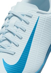 Białe buty sportowe z teksturowanym wierzchem, odważnym niebieskim znakiem Nike i wąskimi, jasnoniebieskimi sznurowadłami. Gumowa podeszwa z bieżnikiem.