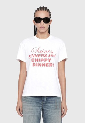 Person wearing black sunglasses, white t-shirt with red text "Saints, Sinners and Chippy Dinners," and blue jeans, standing against a gray background.