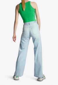 Lys blå, vide jeans med høj talje, baglommer og frayed kanter, parret med en stram grøn tanktop og grå sportssko.