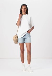 Vit t-shirt med kort ärm och en lätt rund halsringning, i kombination med ljusa denimshorts och en beige axelväska. Vita sneakers fulländar looken.