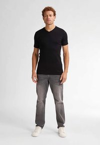 Tricou negru cu mâneci scurte și decolteu în V, confecționat din bumbac moale, asortat cu blugi gri și adidași albi. Design simplu, cu o siluetă mulată.