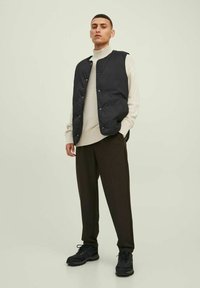 Chaleco acolchado negro sobre un suéter crema, combinado con pantalones oscuros y zapatillas negras. Textura suave con detalle de botones en el chaleco.