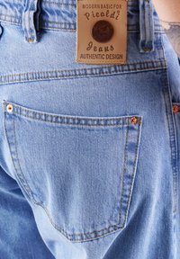 Helles blaues Denim-Jeans mit einer rechteckigen Tasche und kupferfarbenen Nieten. Besitzt ein Lederetikett mit "Picaldi Jeans" und "Authentic Design."