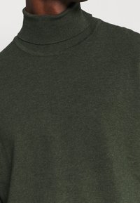 Tmavozelený rolákový svetr z měkkého pleteného materiálu. Má přiléhavý střih s žebrovaným límcem a hladkou texturou.