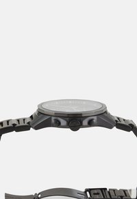 Orologio in acciaio inossidabile nero con quadrante tondo, bracciale flessibile e due pulsanti laterali. Presenta una superficie testurizzata e indicatori dell'ora chiari.