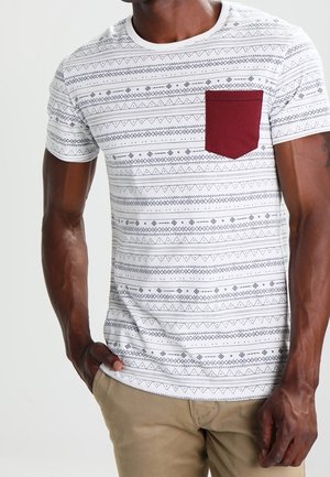 White t-shirt featuring a geometric pattern in navy and blue, with a maroon chest pocket. Short sleeves and a round neck design.