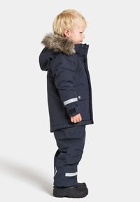 Veste d'hiver bleu marine avec capuche doublée en fausse fourrure, bandes réfléchissantes et pantalon assorti. Matériau épais et isolé avec une coupe ajustée.