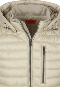 Lichtbeige gewatteerde jas met een hoge kraag, ritssluiting aan de voorkant, twee zijzakken en een verstelbare capuchon met trekkoorden.