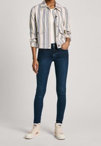 Chaqueta de botones a rayas en crema, azul y gris; combinada con jeans skinny azul oscuro y zapatillas altas beige claras.