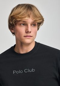 Svart sweatshirt med rund hals och en texturerad "Polo Club"-logotyp i grått över bröstet. Tillverkad av bomull med en slät yta.