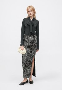Crna bluza dugih rukava s detaljem mašne, uparena sa crnom suknjom s šljokicama i prorezom do bedra, te kremastim clutch torbicom.