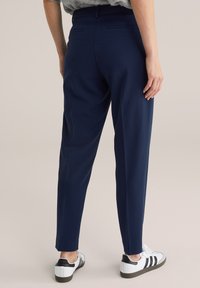 Pantalones de corte ajustado en azul marino con una textura suave, piernas cónicas y bolsillos traseros, combinados con zapatillas blancas con detalles en negro.