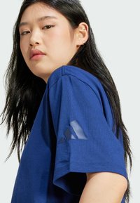 Blå bomulds t-shirt med rulleærmer, rund halsudskæring og et tekstureret Adidas-logo på ærmet. Blødt stof med en glat overflade.