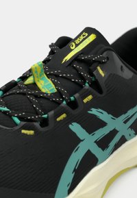 Sort løbesko med en struktureret overdel, akvamarine accentdesign og klare gule snørebånd. Har en polstret sål og forstærkede snørehuller.