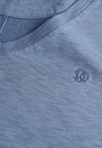 Lyseblå, kortærmet t-shirt med v-hals. Har et struktureret materiale og et broderet logo i det øverste højre hjørne.