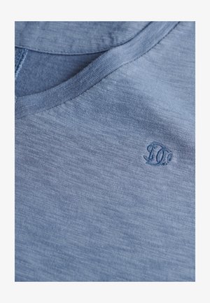 Hellblaues, kurzärmeliges T-Shirt mit V-Ausschnitt. Besitzt einen strukturierten Stoff und ein gesticktes Logo in der oberen rechten Ecke.