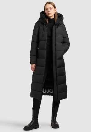 Melnā garā puffer jaka ar kapuci, kas aprīkota ar quilted daļām, sānu kabatām un rāvējslēdzēju. Gluda ārpuse un silta izolācija.