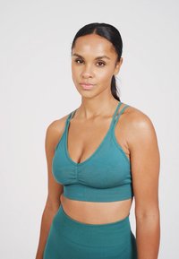 Top corto atlético en color aguamarina con tirantes finos, un diseño ajustado y tela elástica, que presenta un detalle de fruncido en la parte delantera y una banda de soporte.