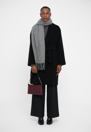 Black belted coat, gray scarf with fringe, gray sweater, wide black trousers, and heeled black boots. Holding a small burgundy handbag.