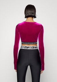 Sopii pitkähihaisen magentan sametista valmistetun ykkösen, jossa on lyhennetty muoto; yhdistetty korkeavyötäröisiin mustiin leggins-leggingseihin, joissa on kontrastivärinen vyötärö.